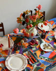 Decorative table setting with a colorful tablecloth, plates, cutlery, and a vase of flowers.