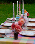 Decorated outdoor table with colorful checkered tablecloth, floral arrangements, and tall candles.