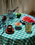 Table setting with coffee, fruit, and watermelon on a green checkered tablecloth with murano glassware