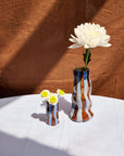 Two vases with flowers on a checkered tablecloth against a brown textured wall.