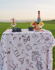 A tablecloth with a pattern of martinis, oysters, wine, and playing cards displayed on a table outdoors.
