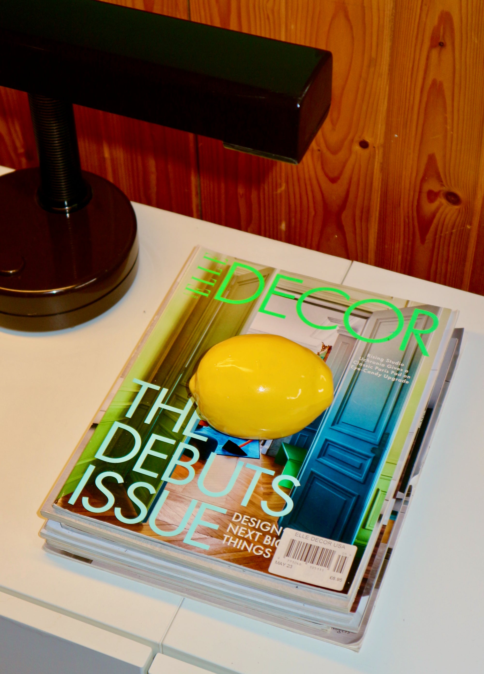 Decor magazine with a lemon on the cover on a table next to a lamp.