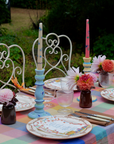 Decorative outdoor table setting with colorful plates, candles, and flowers.