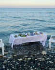 Marla Primrose Embroidery Meditarrean Tablecloth Dining table set with food on a white cloth by the ocean