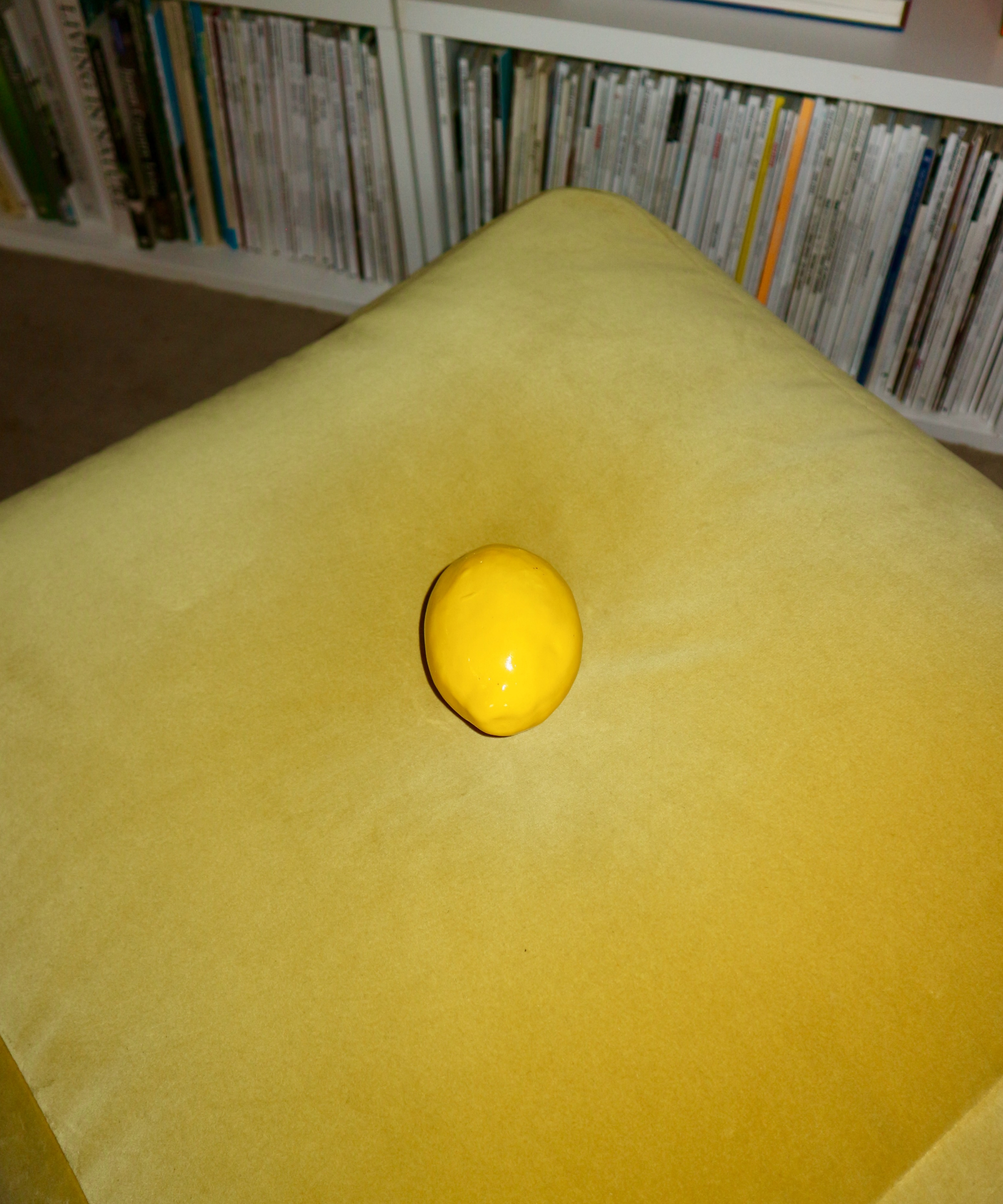 Yellow lemon on a yellow cushion with a bookshelf in the background