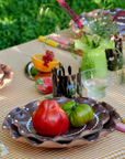 Decorative table setting with tomatoes, flowers, and glasses on a checkered tablecloth with brown ripple small plate.