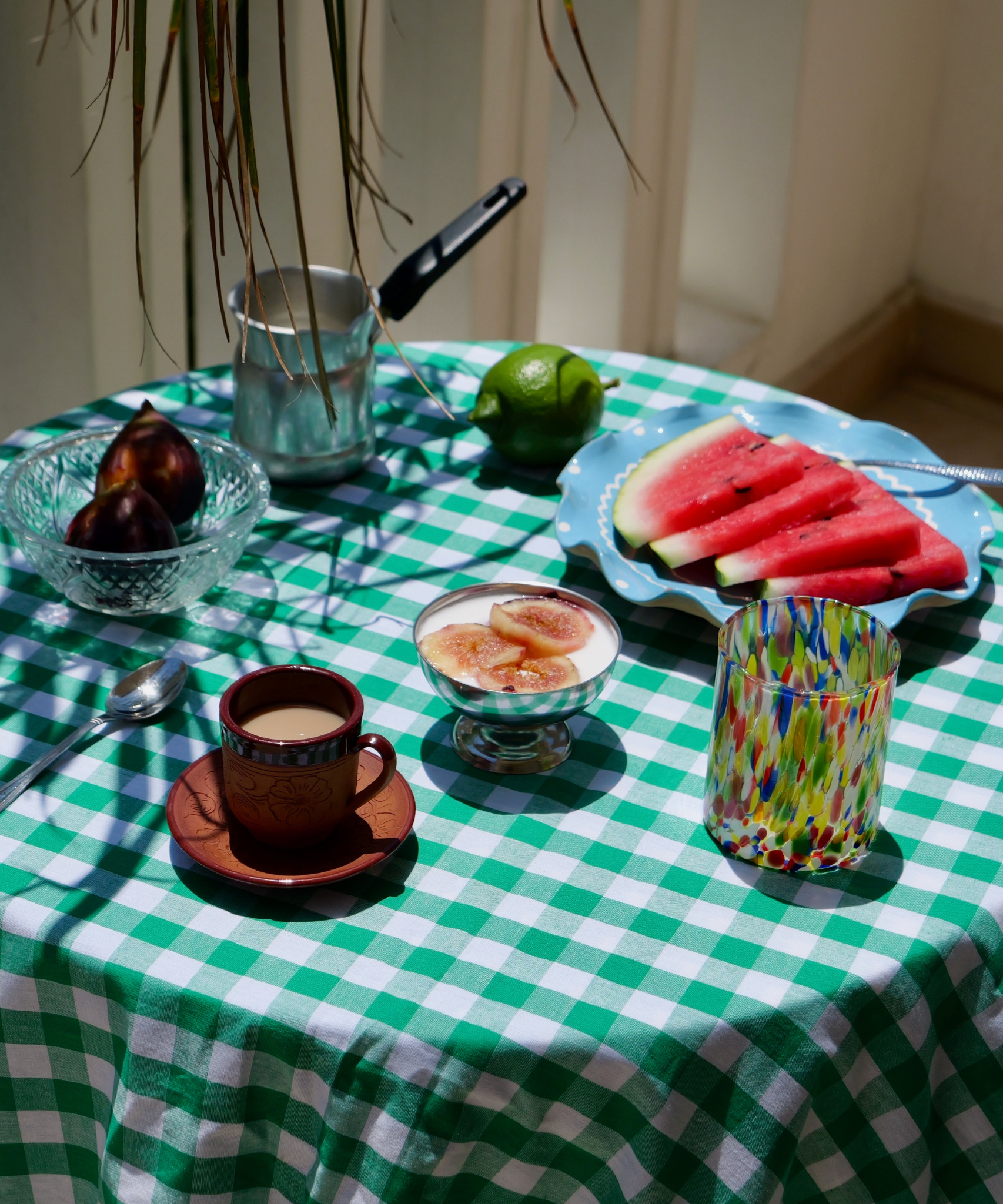 Table setting with coffee, fruit, and watermelon on a green checkered tablecloth with murano glassware