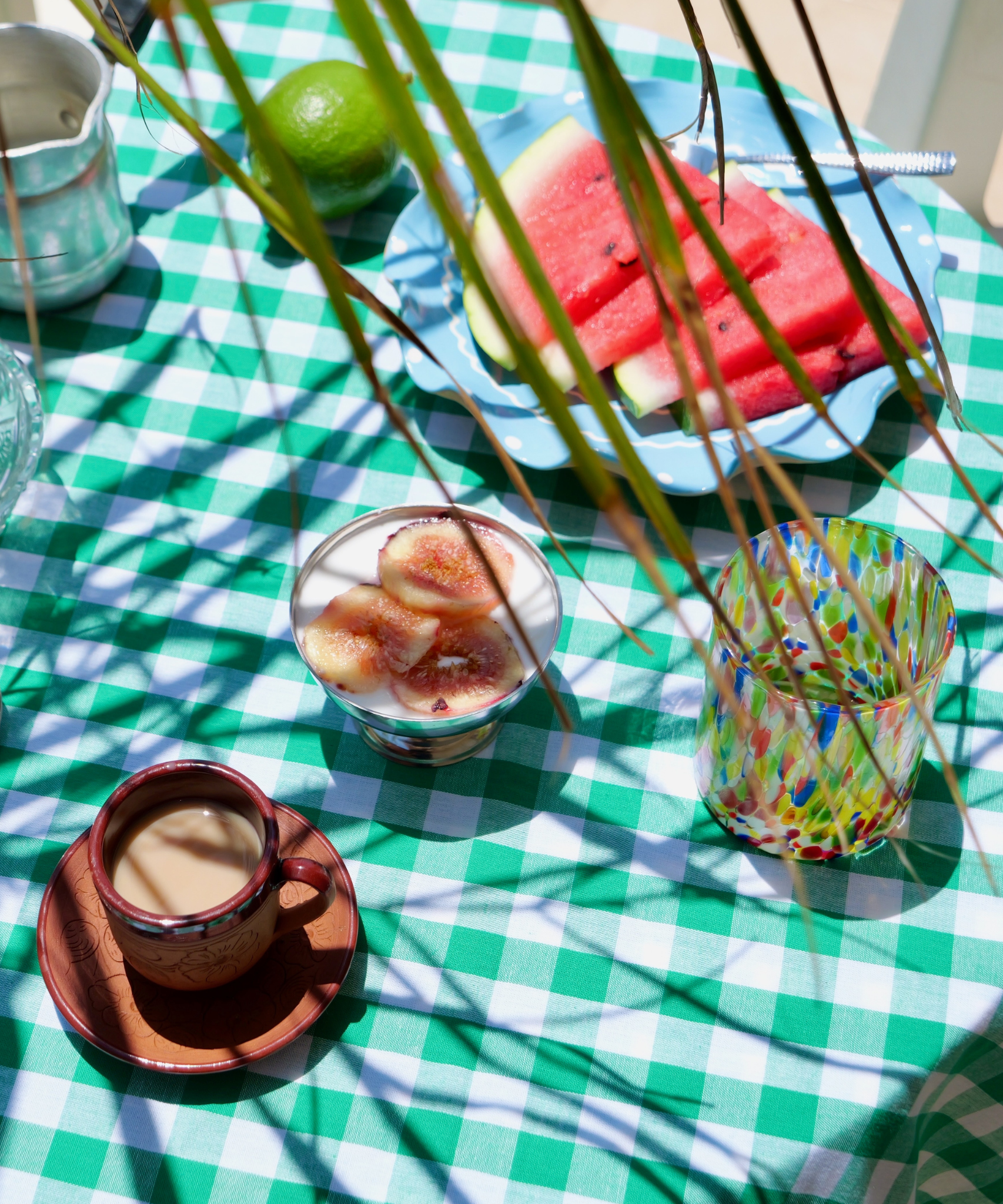 Outdoor setting with a green and white checkered tablecloth, watermelon slices, and a colorful glass.