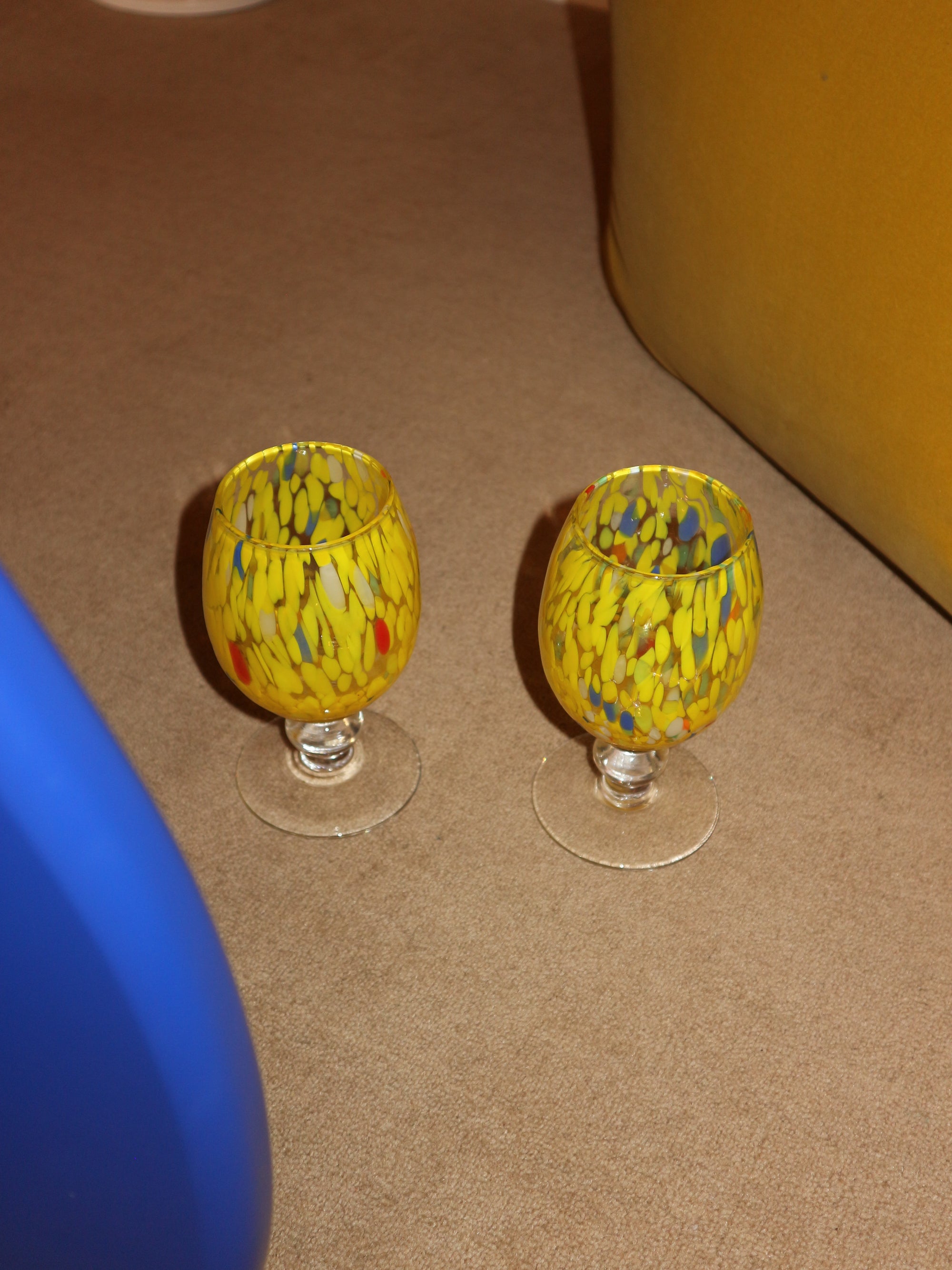 Two yellow glass knobs with a colorful pattern on a brown surface.