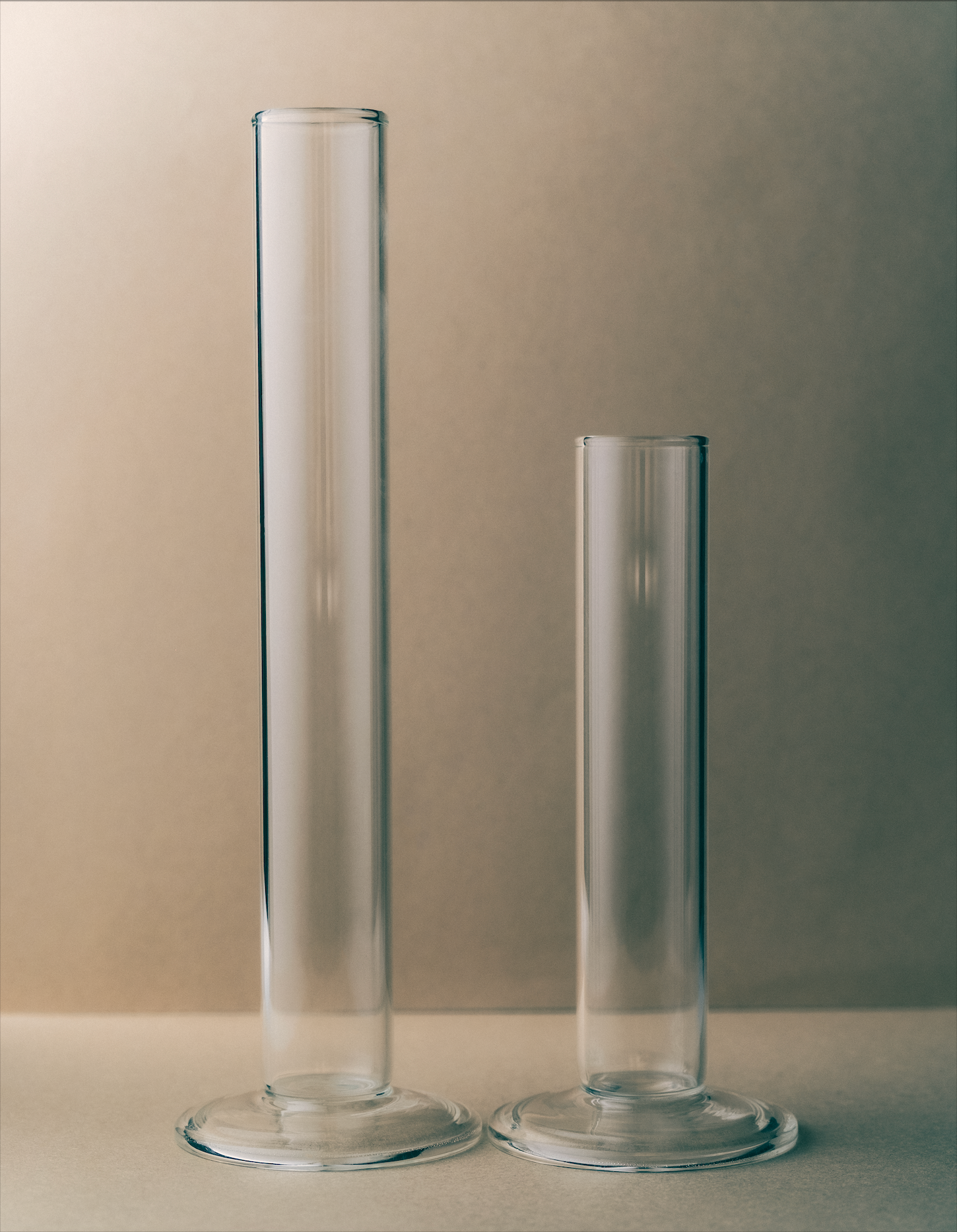 Two clear glass cylinders on a neutral background