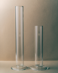Two clear glass cylinders on a neutral background