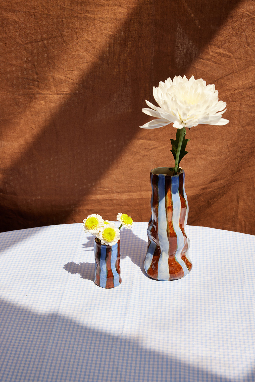 Two vases with flowers on a checkered tablecloth against a brown textured wall.